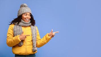 Look There Concept. Black Woman In Winter Jacket Pointing Fingers Aside Advertising Something Standing On Purple Background. Winter Advertisement. Studio Shot, Panorama With Empty Space For Text photo