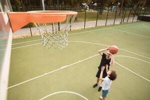 Above top high angle view of boy playing basketball with his dad at playground court outdoors, man throwing ball to hoop. Happy family spending time together and celebrating father's day photo