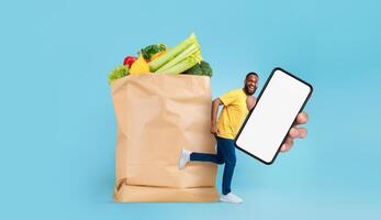 A customer holding a smartphone runs alongside a large paper bag filled with fresh groceries. The bright blue background emphasizes the convenience of shopping in today's new normal. photo