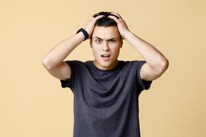 Disappointment, failed, loss and freaking out. Upset shocked zoomer man in brown t-shirt with open mouth, holding his head with hand, isolated on beige background, studio shot, free space photo