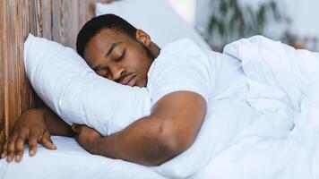 African American Man Sleeping Hugging Pillow Resting Lying With Eyes Closed In Comfortable Bed In Bedroom At Home. Rest And Napping, Recreation, Bedtime Concept. Panorama photo