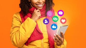 African Woman With Smartphone Networking Using Social Media, Commenting And Texting In Mobile App Standing Over Yellow Studio Background. Phone User Concept. Collage With Icons, Cropped photo