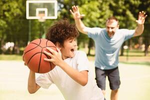 Family Time. Son and dad enjoying basketball game with fun, man running to his kid, trying to steal the ball photo