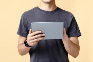Work of freelancer or blogger with mobile gadget and application. Young man with smart watch typing on digital tablet, isolated on beige background, studio shot, free space, cropped, panorama photo