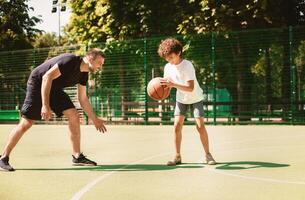 Healthy Lifestyle. Team of two players enjoying basketball game on a sports ground, kid leading the ball photo
