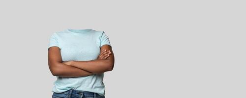 A headless person stands confidently with arms crossed, showcasing a casual blue shirt. The background is a plain, light color, creating a focused and isolated aesthetic for lifestyle portrayals. photo