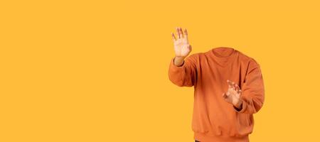 A headless figure wearing an orange sweatshirt gestures with hands in a vibrant yellow setting. This collage-style design emphasizes isolation with bright colors and empty space. photo