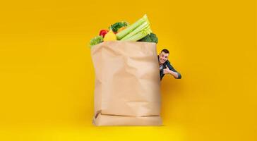 A customer stands next to a large paper bag filled with fresh groceries, showcasing vibrant fruits and vegetables. photo