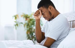 Male Depression. Depressed African American Guy Sitting In Bed Thinking About Problems In Bedroom At Home. Unhappy And Stressful Life And Troubles Concept. Empty Space For Text photo