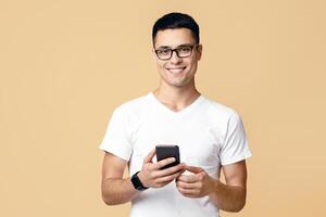 Man look at smartphone, feel joyful reading good news. Smiling young blogger student in glasses, white t-shirt with smart watch search information and looking at camera, isolated on light background photo