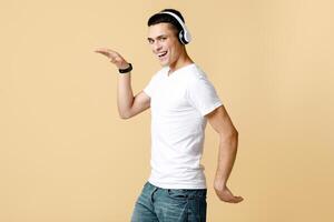 Dancing and fun with favorite music. Happy excited young man student in white t-shirt with modern headphones dancing funny dance at free time, isolated on light background, side view, empty space photo