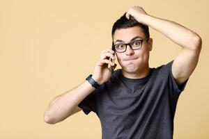 Problems at work, difficult question or hard choice. Confused shocked man in glass alarmed, talking on phone with boss and scratching head, isolated on light background, empty space, studio shot photo