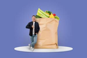 A cheerful customer stands beside a large paper grocery bag filled with fresh vegetables and fruits. This captures the essence of shopping in the new normal of isolated delivery. photo