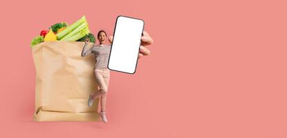 A customer stands next to a paper bag filled with fresh groceries while holding a smartphone. This reflects the new normal of shopping and delivery in a modern lifestyle. photo