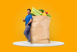 A satisfied customer stands next to a large paper bag filled with fresh groceries, showcasing vegetables and fruits. The bright background emphasizes the new normal of shopping. photo