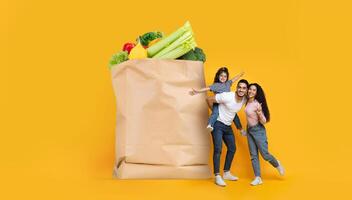 A family of three poses happily with a large paper grocery bag filled with fresh produce. Their joyful expressions reflect a positive experience of shopping together in a vibrant atmosphere. photo