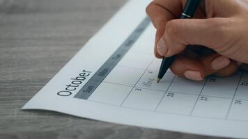 A young professional is using a pen to write on a calendar for October, organizing her tasks and appointments in a modern office setting. She focuses on her upcoming work week, ensuring productivity. photo