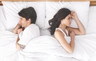 Relationship problems. Upset couple ignoring each other, lying back to back in bed, top view photo