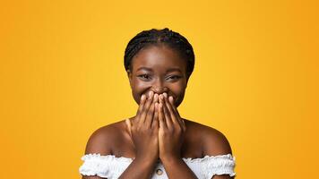 Laughter. Cheerful Black Lady Smiling And Covering Mouth With Hands In Happy Excitement, Emotionally Reacting To Pleasant Surprize, Having Positive Mood, Isolated On Yellow Background, Copy Space photo