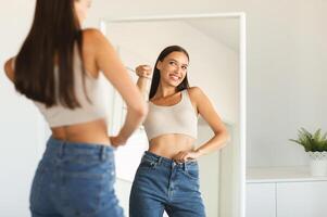 Self confidence concept. Happy caucasian lady pointing finger at her reflection in mirror, having fun while posing after great weight loss, free copy space photo