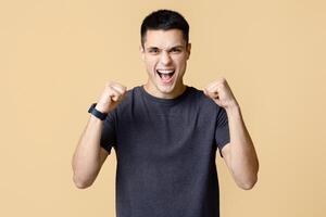 Success, victory and luck in business or work. Joyful young man with smart watch looks at camera and expresses emotions of win and success, isolated on light background, empty space, studio shot photo
