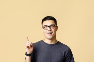 Smart student model ready to learn and shocked by offer. Surprised young zoomer guy with open mouth in glasses show thumb up to empty space for advertising, isolated on light background, studio shot photo