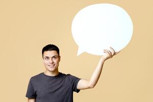 Man thoughts, man opinion and good review. Pensive young guy student with smart watch hold abstract space, bubble for words, isolated on light sand background, empty space, studio shot photo