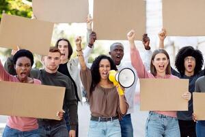Young mixed race woman with megaphone leading a group of demonstrators with blank placards on the street. International group of people protesting for human rights, showing empty boards photo