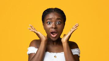 OMG. Astonished Black Woman Shouting In Excitement, Holding Hands Near Face, Surprised African Lady Looking At Camera With Opened Mouth, Posing In Studio Over Yellow Background With Copy Space photo