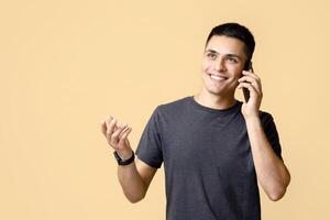 Ideas for business, modern work and communication from home. Happy cheerful young man talking on phone and gesturing, isolated on light sandy background, empty space, studio shot photo