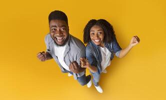 Big Luck. Top view of excited black couple celebrating success or victory with raised hands, clenching fists while standing on yellow background photo