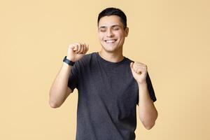 Victory and win dance, positive emotions and great mood. Happy young man student with closed eyes with smart watch expresses success and happiness, isolated on beige background, studio shot photo