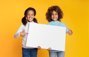 Child girls holding empty banner and pointing on it, copy space, yellow background photo
