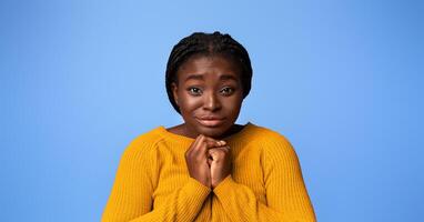 Please, Buy. Cute black woman pleading and asking for something with clasped hands, young african lady with begging face expression posing over purple studio background, looking at camera, copy space photo
