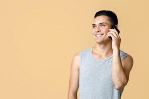 Modern communication and important call during self-isolation at home. Cheerful handsome man student in casual speaks on phone and looks at empty space, isolated on light background, studio shot photo
