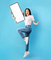 Advertisement for mobile application. Excited young lady jumping over blue studio background, showing modern smartphone with empty screen, mockup for app. Collage photo