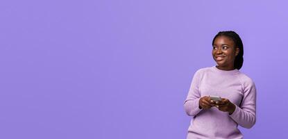Portraif Of Smiling African American Lady Holding Smartphone And Looking Aside At Copy Space On Purple Background With Interest, Curious Black Woman With Cellphone Enjoying Mobile Offer photo