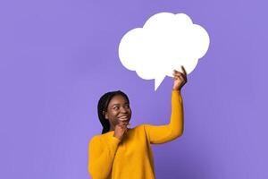Idea Concept. Pensive black lady holding and looking up at blank speech bubble with copy space for your text or design, curious african american woman posing over purple studio background photo