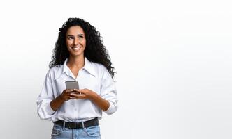 Mobile Offer. Pensive Young Woman Holding Smartphone And Looking Away At Copy Space On Yellow Background, Browsing Internet, Checking New App, Messaging With Friends, Enjoying Modern Communication photo