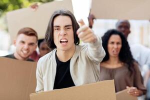 Angry guy leading multiracial group of protestors, pointing at camera. Millennial men and women different nationalities striking on street, holding empty boards, protesting against racism photo