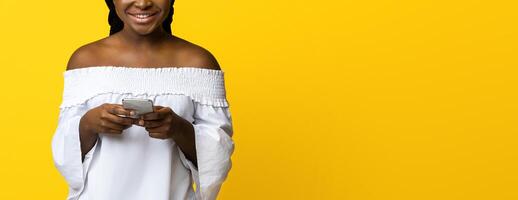 Mobile Communication. Portrait Of Happy Young Black Woman Holding Smartphone And Smiling At Camera, Browsing Internet Or Messaging, Using New Application, Posing On Yellow Studio Background photo