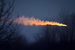 Fiery Meteor Streaking Across Twilight Sky with Bare Trees in Foreground photo