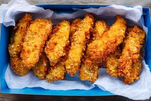 Breaded chicken strips filling a cardboard container with parchment paper photo