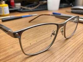 Detail shot of titanium eyeglass frame with wear and discoloration on wooden desk capturing unique craftsmanship photo