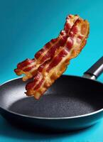 Crispy bacon strip floating above frying pan culinary delight kitchen close-up deliciousness photo