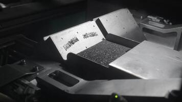 Small black granules on industrial vibrating tray, automated sorting machine process video