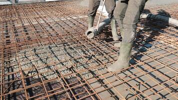Concrete pouring into steel rebar framework, workers in rubber boots at construction site video