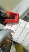 Worker cutting marked metal sheet with an angle grinder producing sparks, close-up of gloved hands using power tool to precisely cut through metal surface in industrial setting. Vertical video