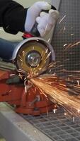 Worker cutting metal with an angle grinder generating vivid bright sparks, close-up of construction worker hands in safety gloves using power tool during industrial fabrication. Vertical video