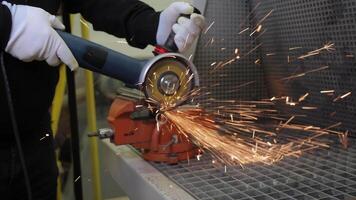 Worker cutting metal with an angle grinder generating vivid bright sparks, close-up of construction worker hands in safety gloves using power tool during industrial fabrication video